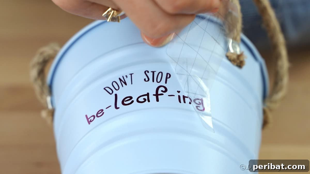 Peeling transfer tape off metal flower pot, revealing the finished design