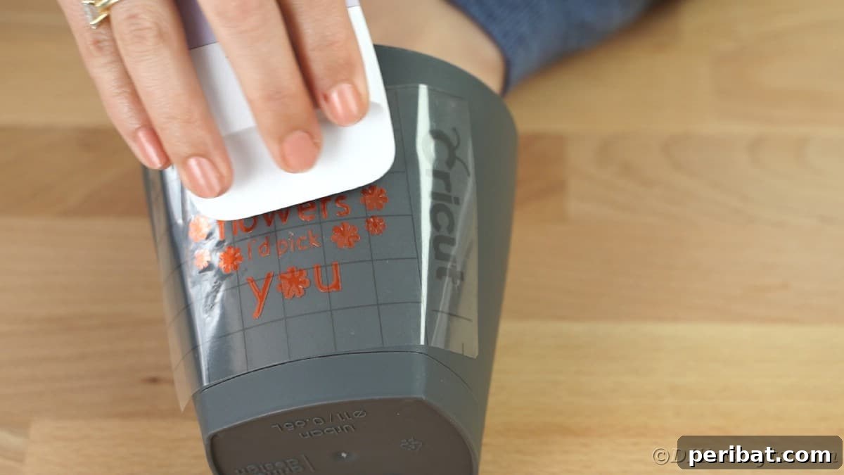 Using scraper tool to press vinyl onto gray flower pot, ensuring secure adhesion