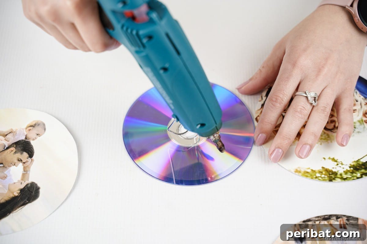 Hands applying hot glue to the surface of an old CD, preparing it for a printed photograph to be attached for the DIY photo ribbon project.