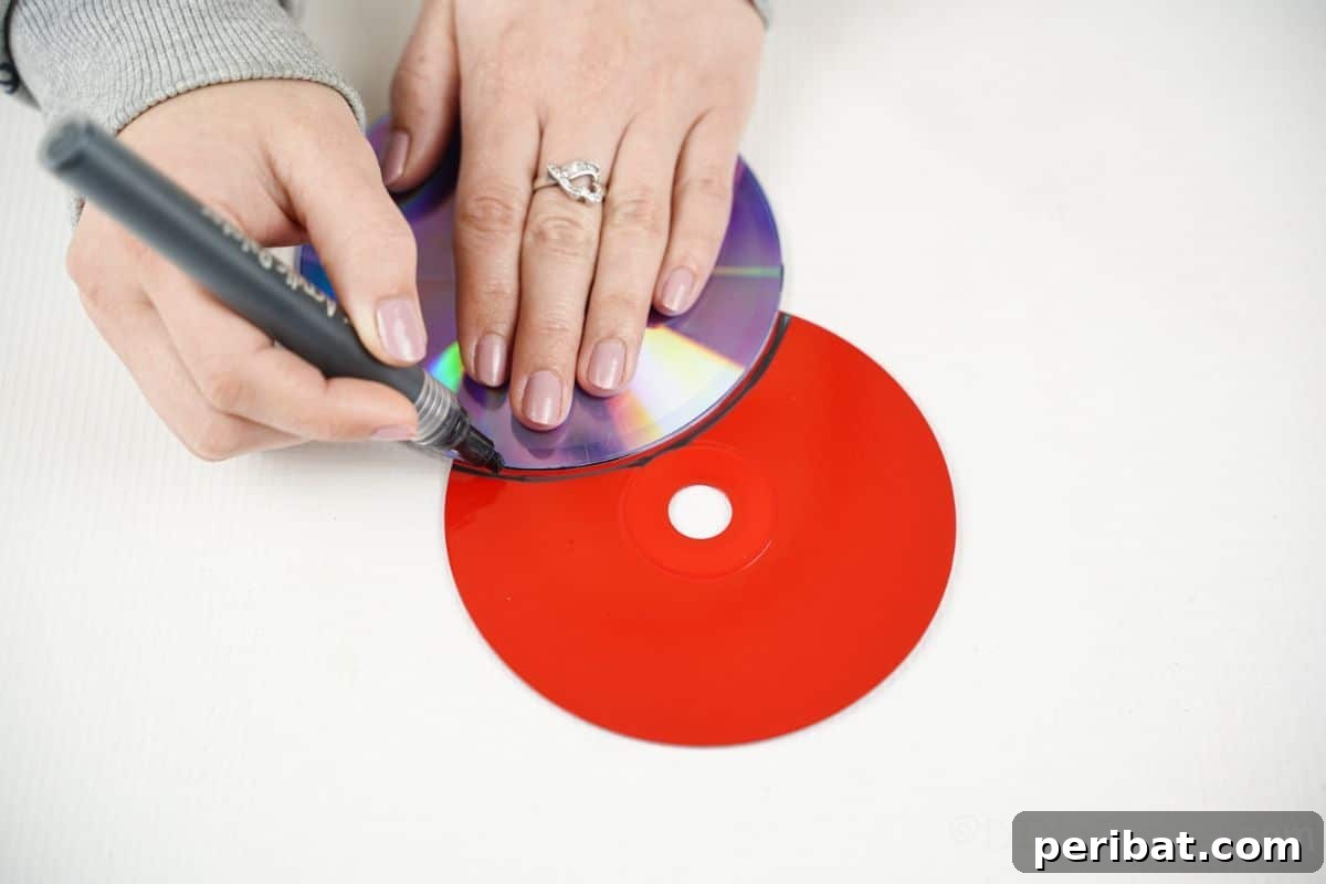 A hand using a black marker to trace a curved line on a painted red CD, outlining the ladybug's head.