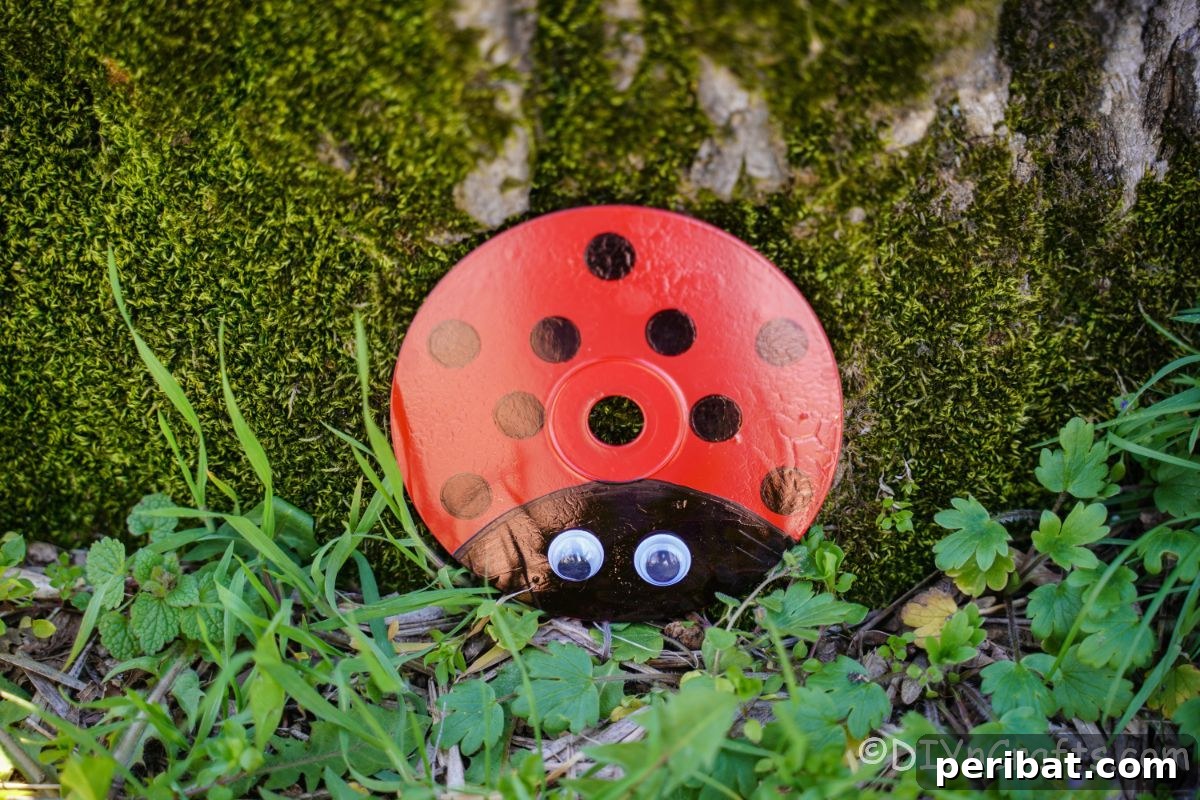 A moss-covered tree serving as a natural backdrop for an upcycled CD ladybug, highlighting its integration with garden elements.