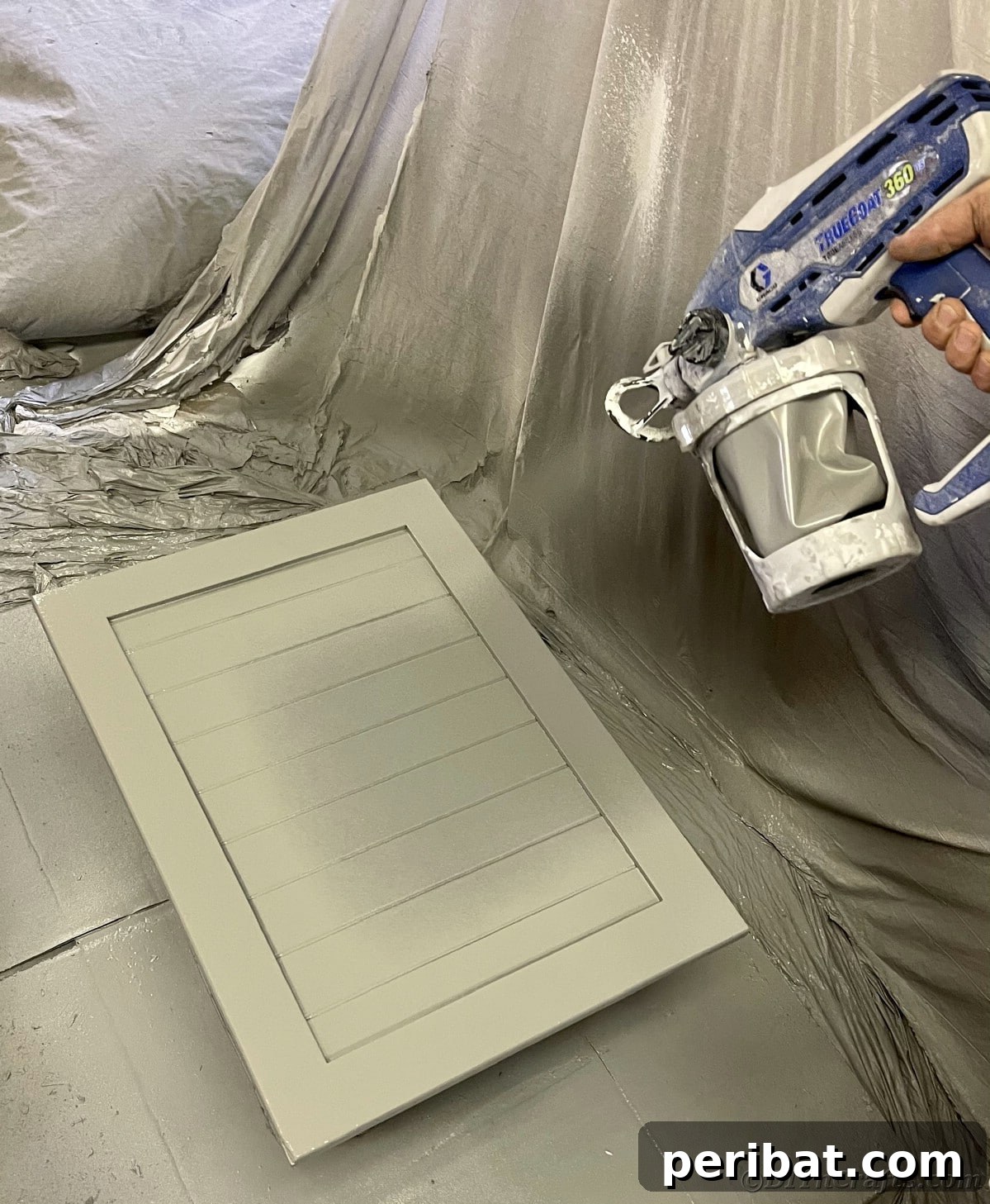 Painting a cabinet door with a sprayer, demonstrating the smooth application technique