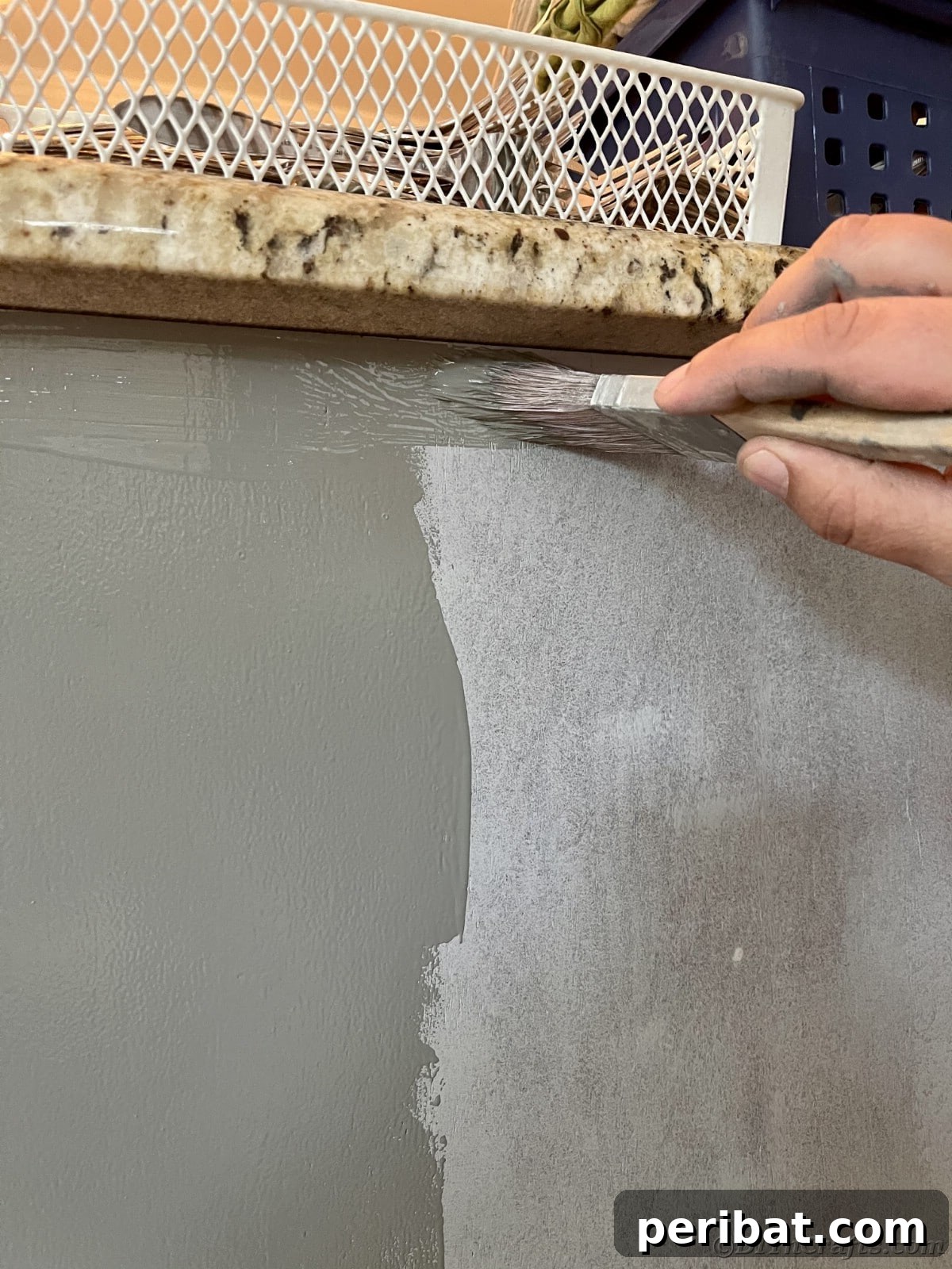 Adding the first coat of gray paint over primer on a kitchen cabinet, showing transformation in progress