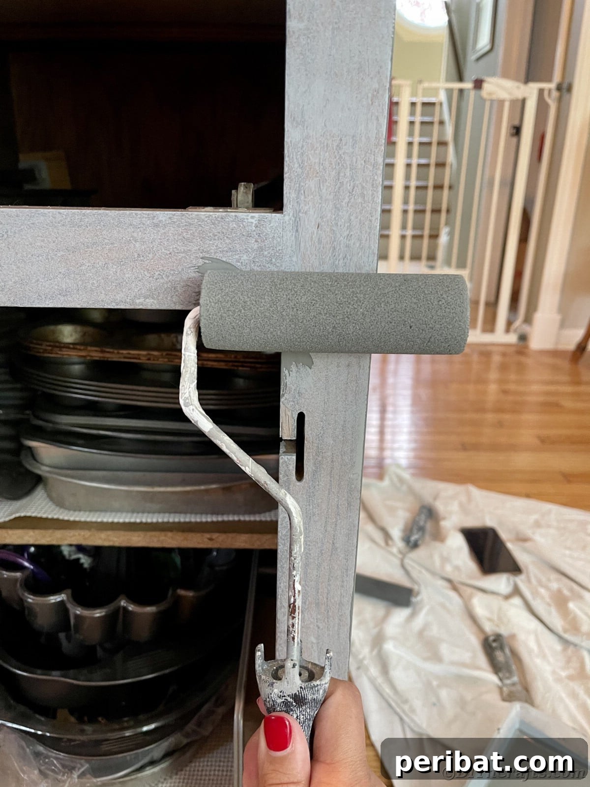Rolling paint on a cabinet base with a paint roller, applying the first coat smoothly