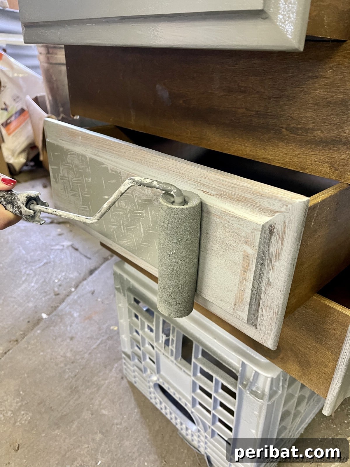 Painting the front of a drawer with a roller, achieving a smooth and even first coat