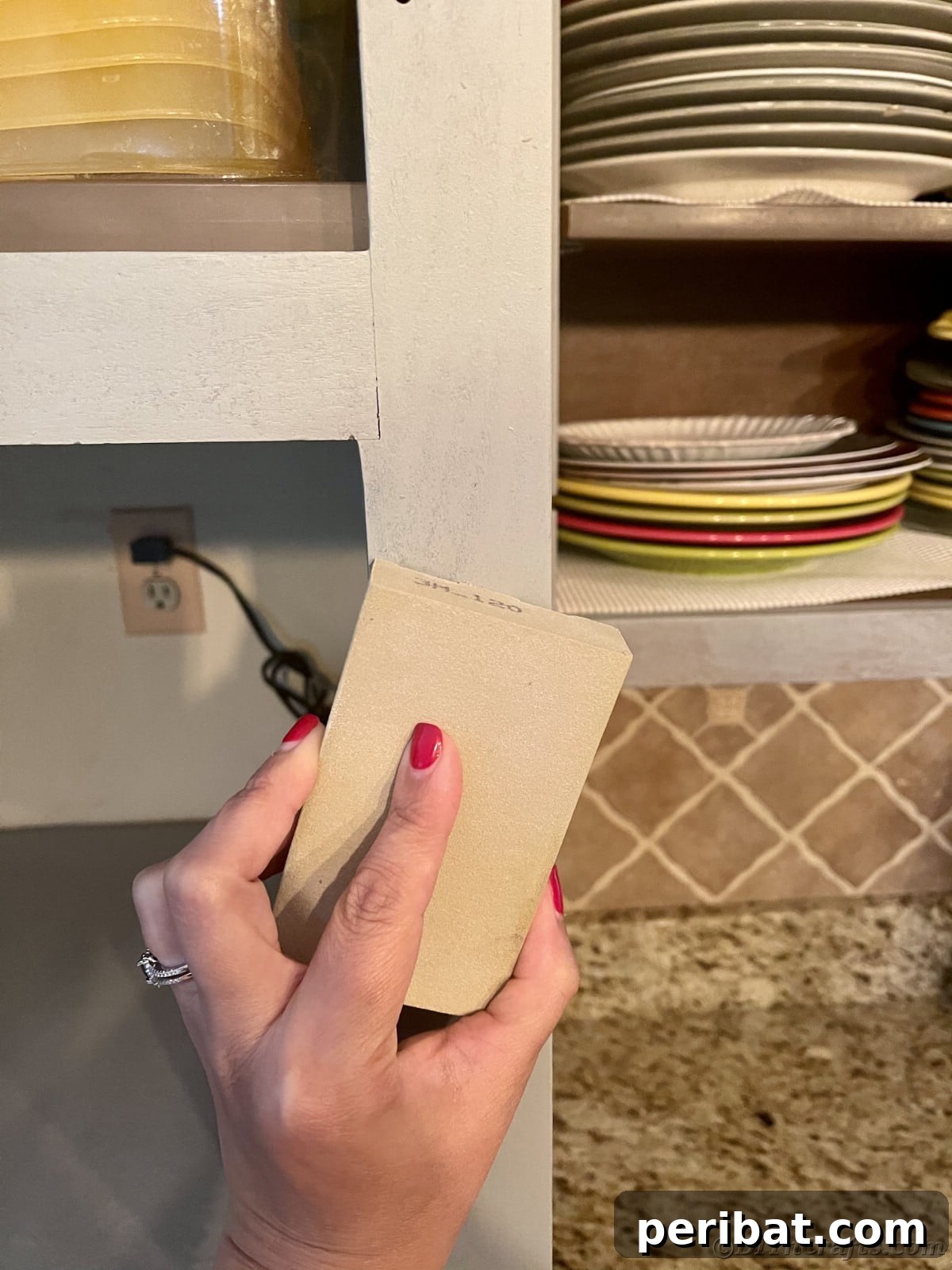 Sanding paint on cabinet bases with a sanding block, smoothing imperfections after the first coat