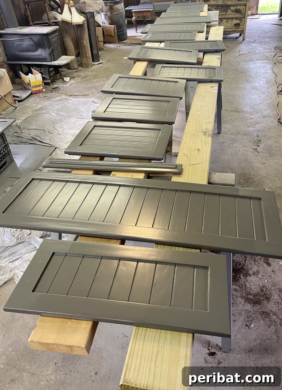 Gray shutter door cabinets lying flat on 2x4s, fully painted and drying in a workspace