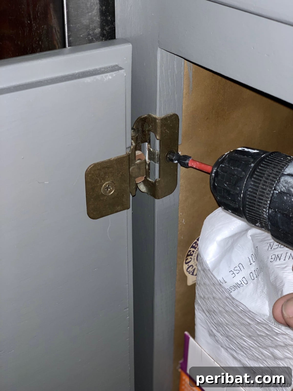 Screwing hardware back onto a cabinet door, showcasing the reassembly process after painting