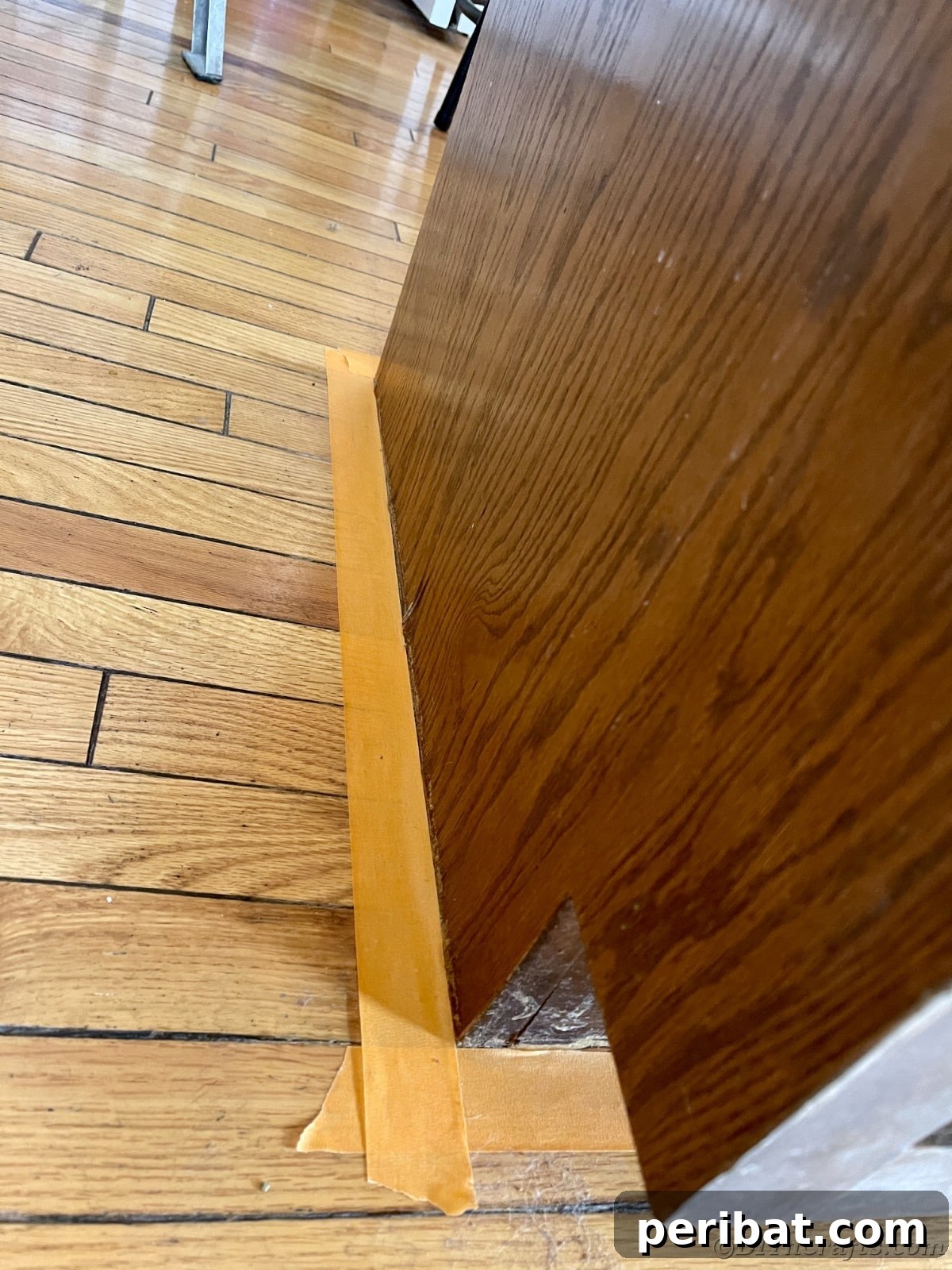 Orange painter's tape applied meticulously on a baseboard, preparing the kitchen for painting