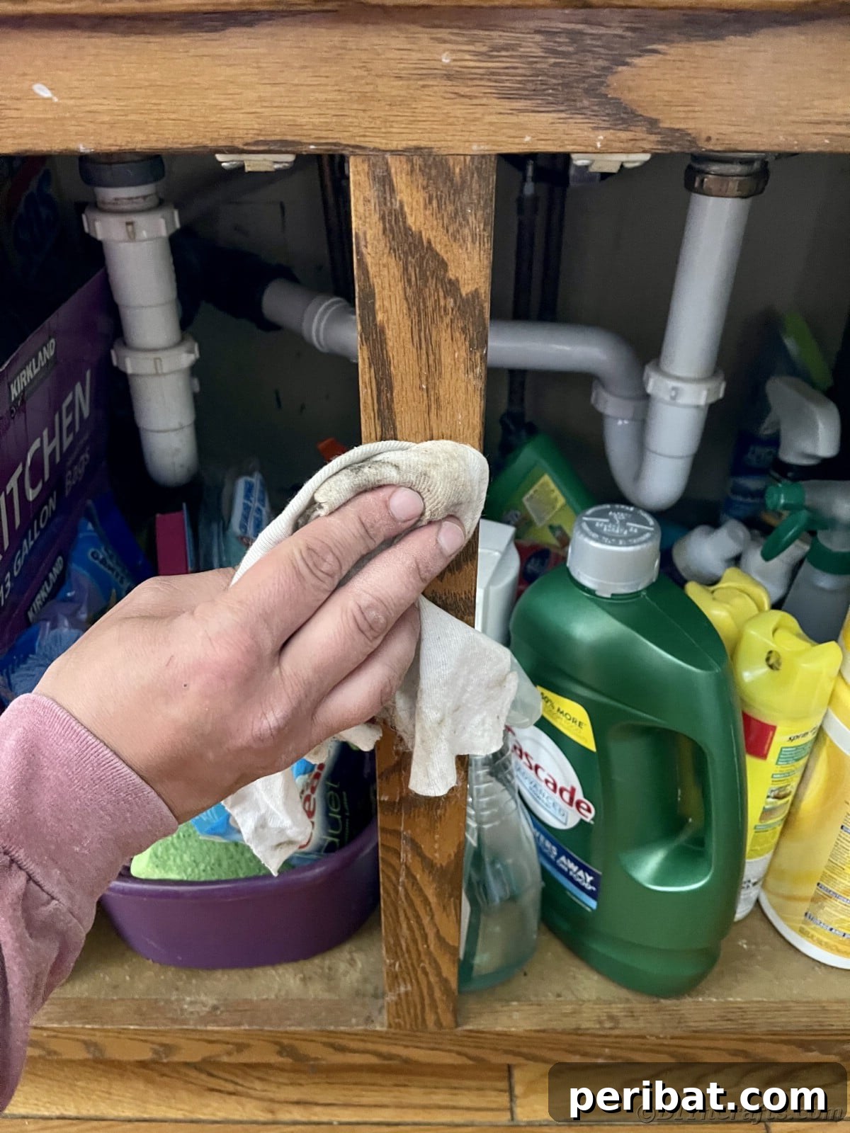 A hand wiping down the cabinet under a sink, demonstrating thorough cleaning before painting