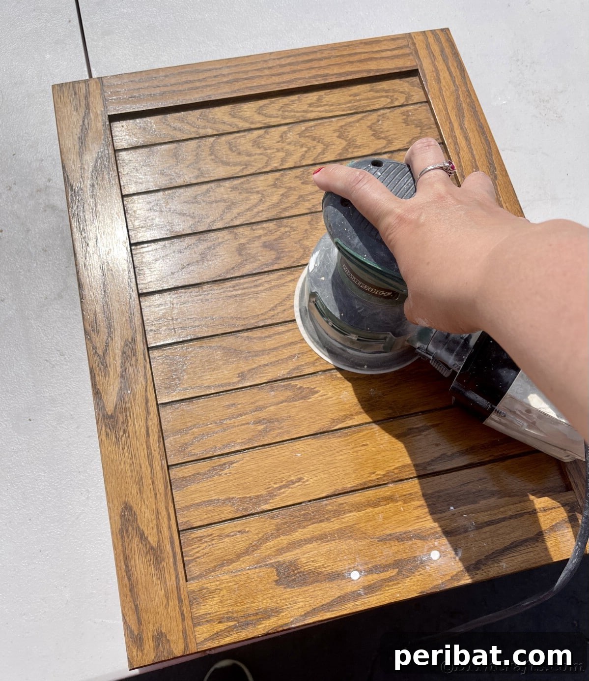 Using an orbital sander on a wood grain cabinet door, preparing it for a smooth finish