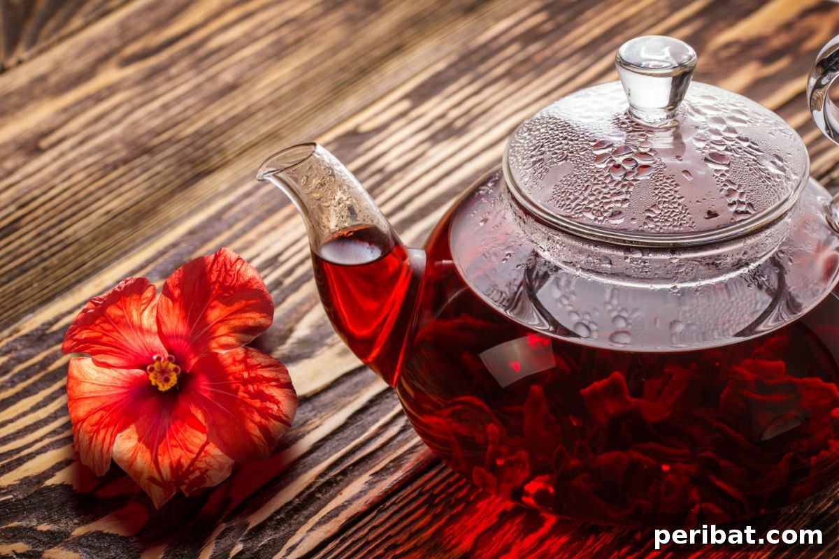 From Garden to Gourmet 10 Edible Flowers to Cultivate 6 A clear teapot filled with hibiscus tea, elegantly placed on a wooden table, accompanied by a fresh red hibiscus flower.