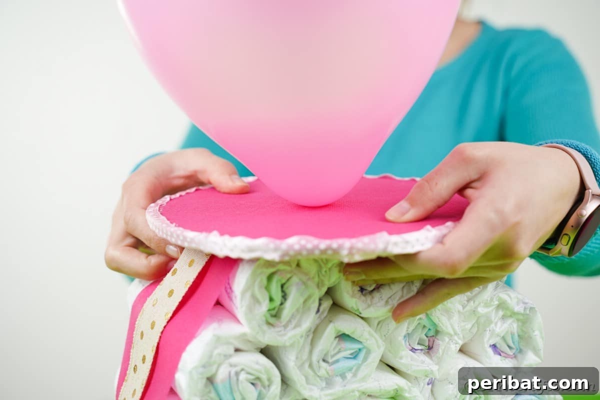 Craft Your Own Darling Pacifier Diaper Cake 12 Woman placing balloon top on stack o diapers