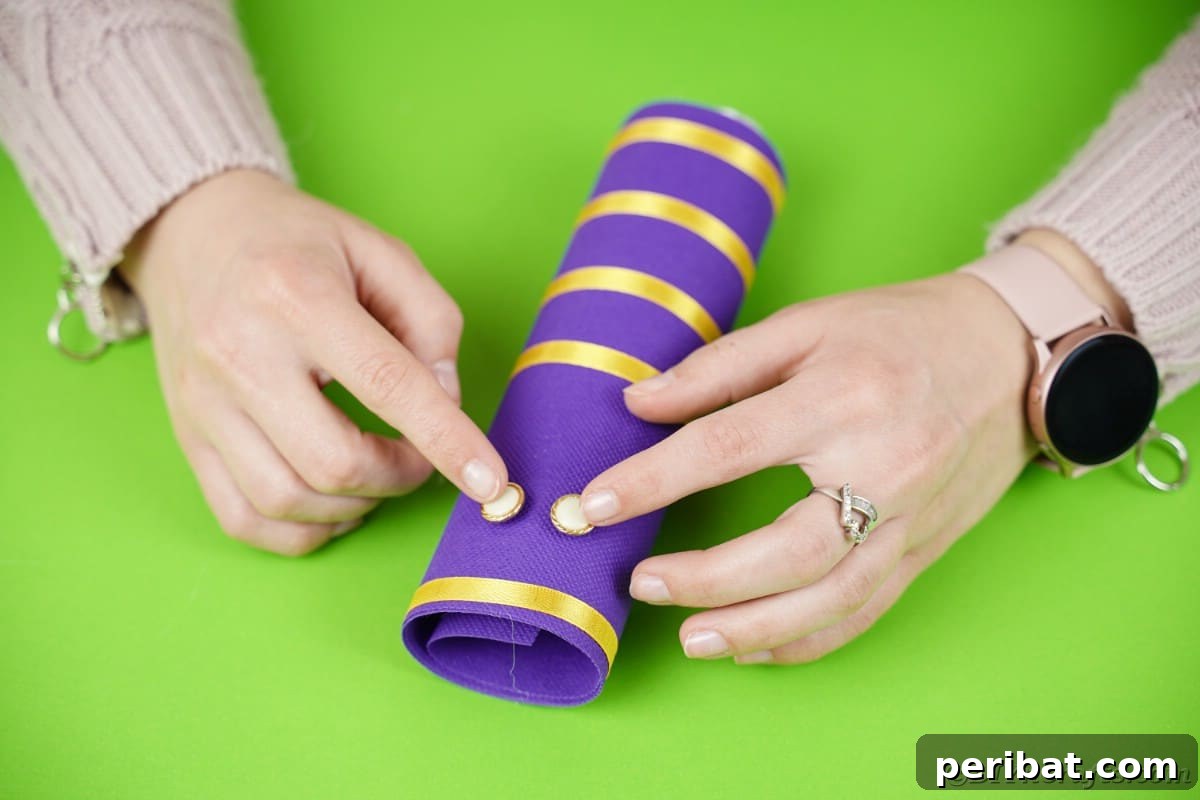 Fluttering Baby Delight: DIY Butterfly Diaper Cake 11 Attaching button eyes to the purple tube with yellow stripes, creating a cute face for the butterfly diaper cake.