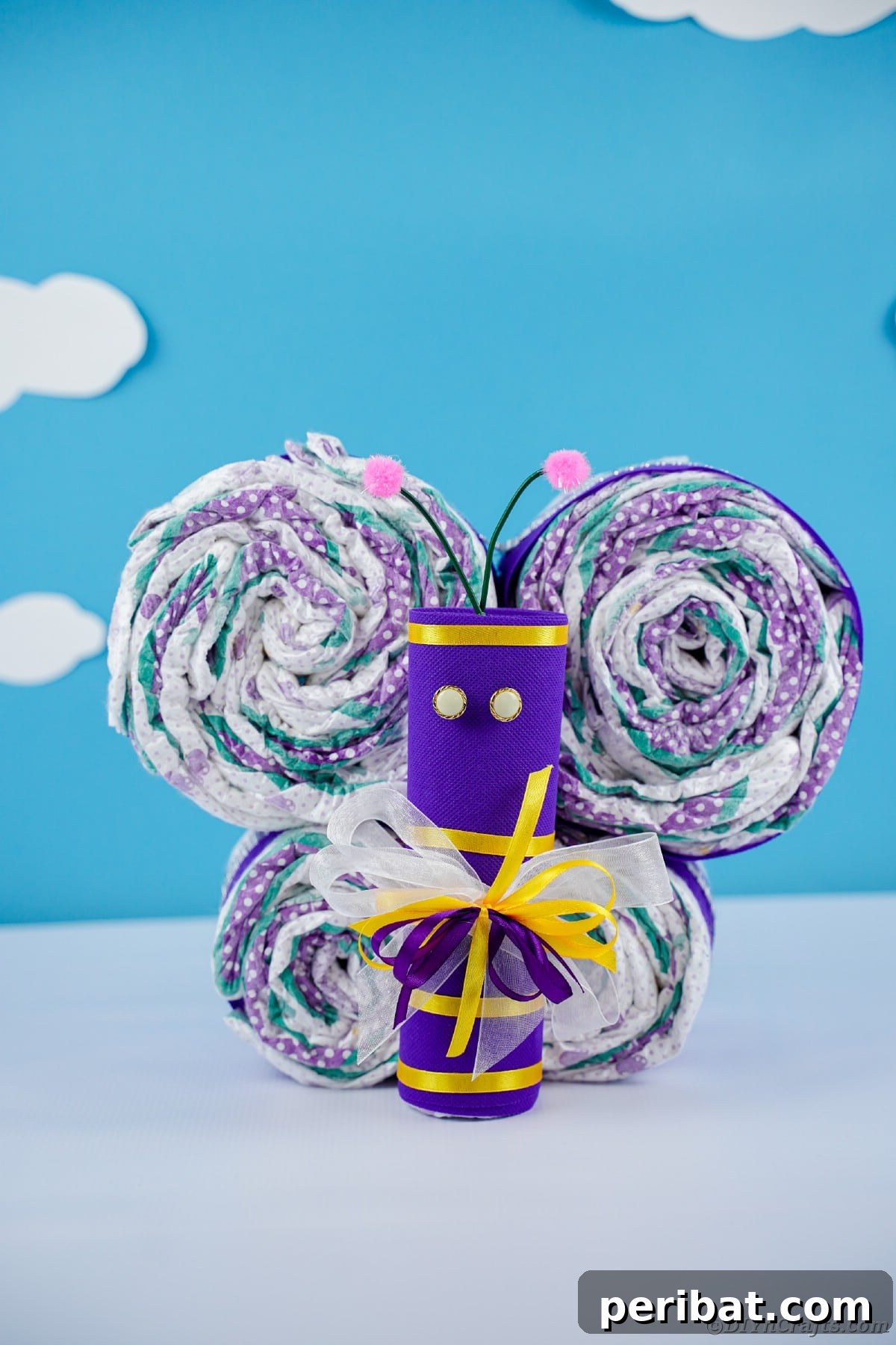 Fluttering Baby Delight: DIY Butterfly Diaper Cake 5 Vibrant purple and yellow diaper butterfly displayed against a charming blue wall with cloud decals, a sweet nursery decor idea.