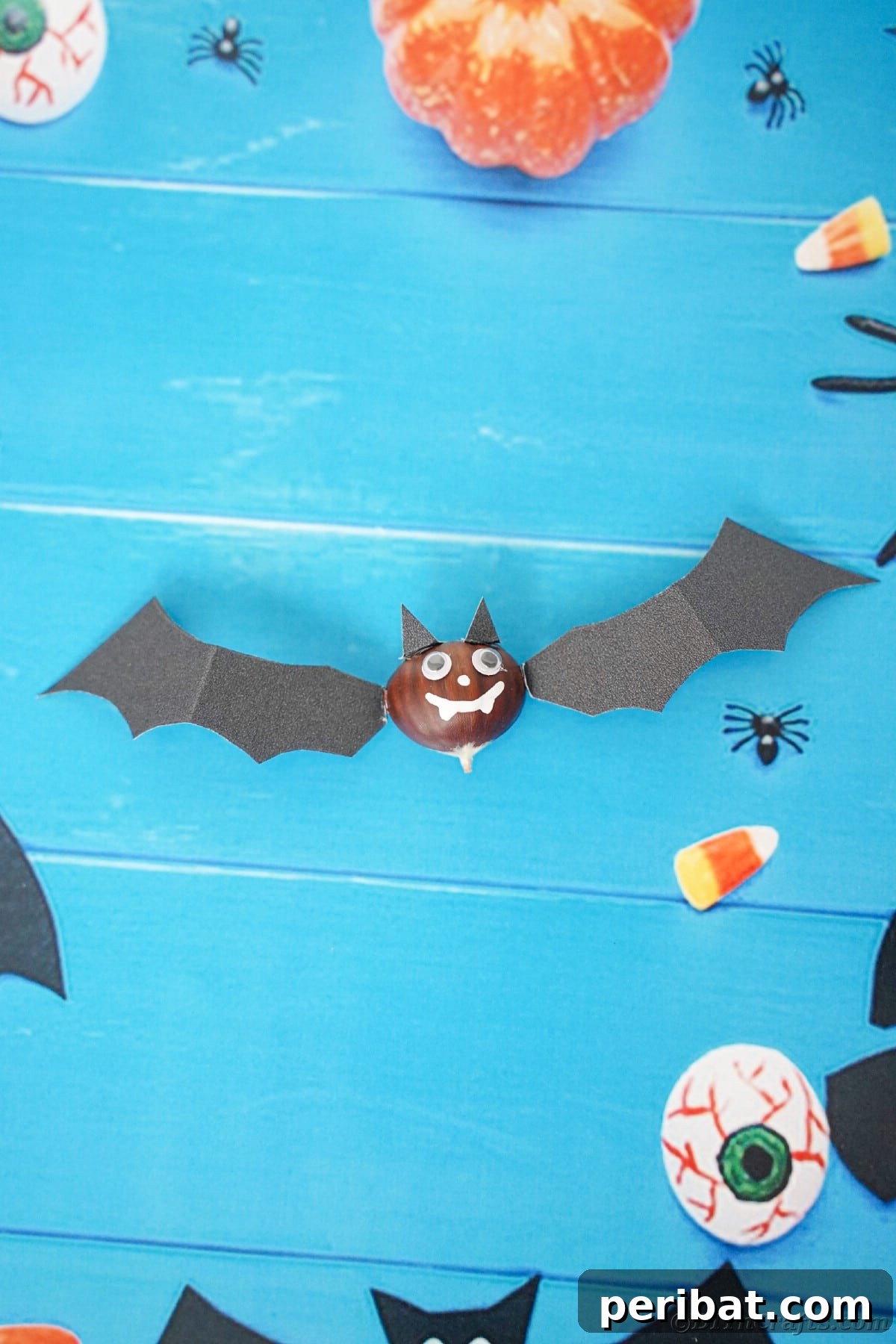 Black bat craft laying on blue paper with fake pumpkins