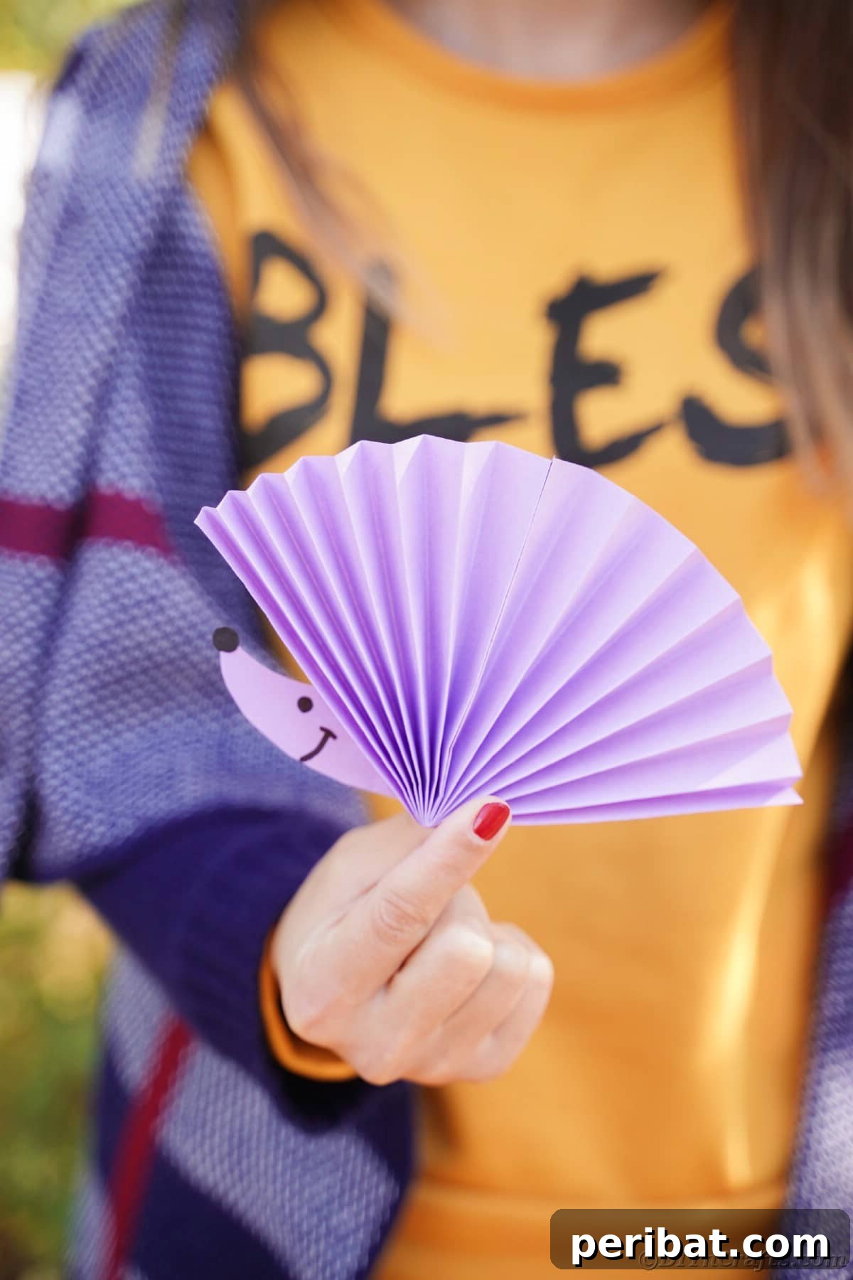 Fan-tastic Hedgehog Craft for Kids 2 A person holding a finished paper fan hedgehog craft, showcasing its purple fan body and cute face.