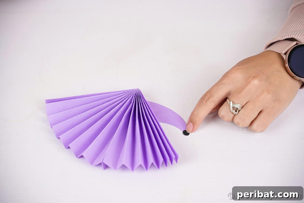 Fan-tastic Hedgehog Craft for Kids 18 A hand gluing the small black paper nose onto the pointed end of the purple paper hedgehog's head, completing its snout.