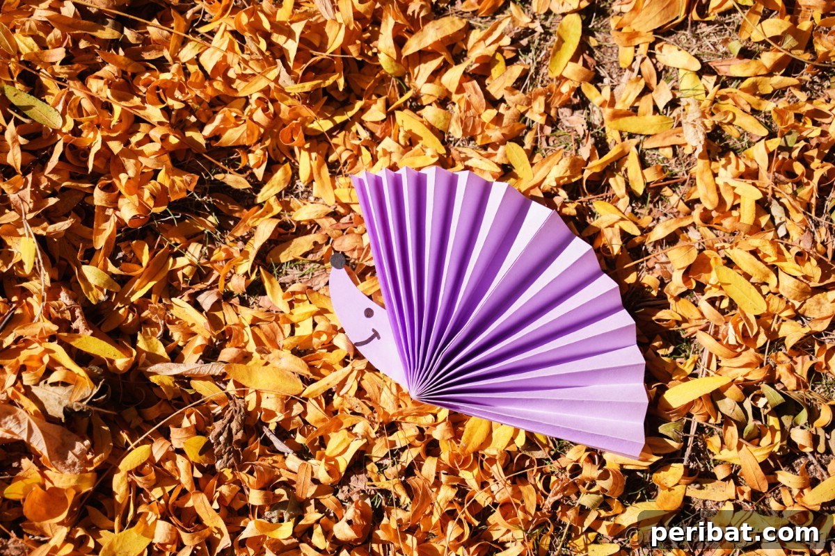 Fan-tastic Hedgehog Craft for Kids 3 A charming paper fan hedgehog resting on a bed of dry autumn leaves, hinting at its seasonal appeal.