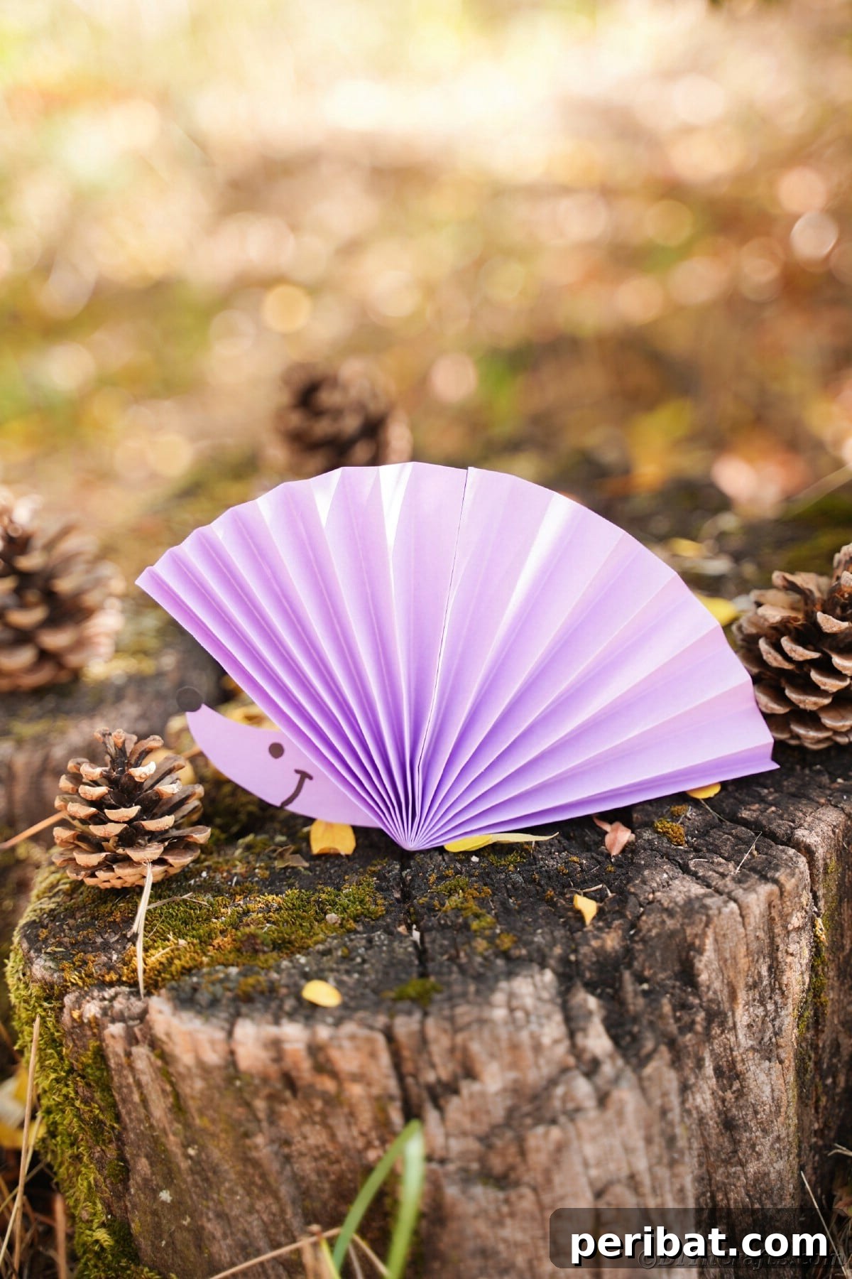 Fan-tastic Hedgehog Craft for Kids 28 A purple paper fan hedgehog with a drawn face sitting on a rustic wooden stump, highlighting its natural setting appeal.