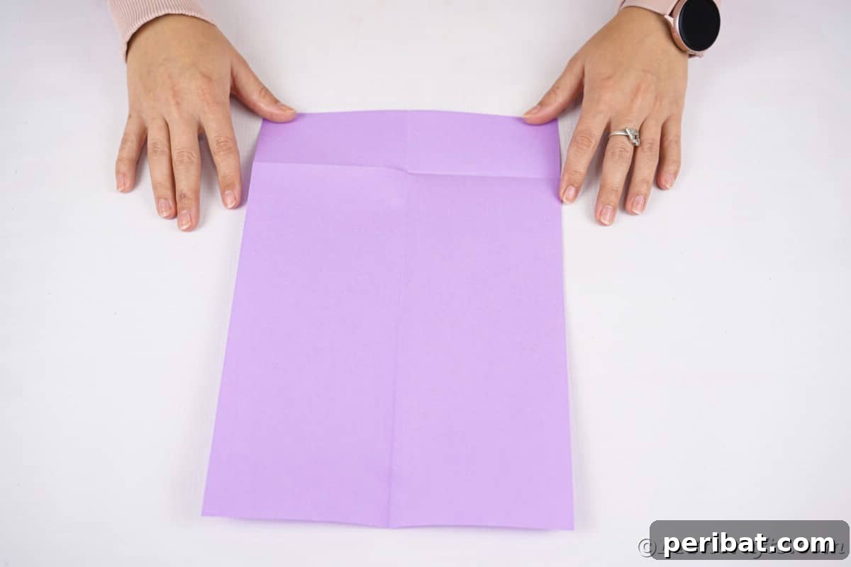 Fan-tastic Hedgehog Craft for Kids 9 Hands demonstrating the initial horizontal fold of the purple craft paper, a key step in creating the hedgehog body.
