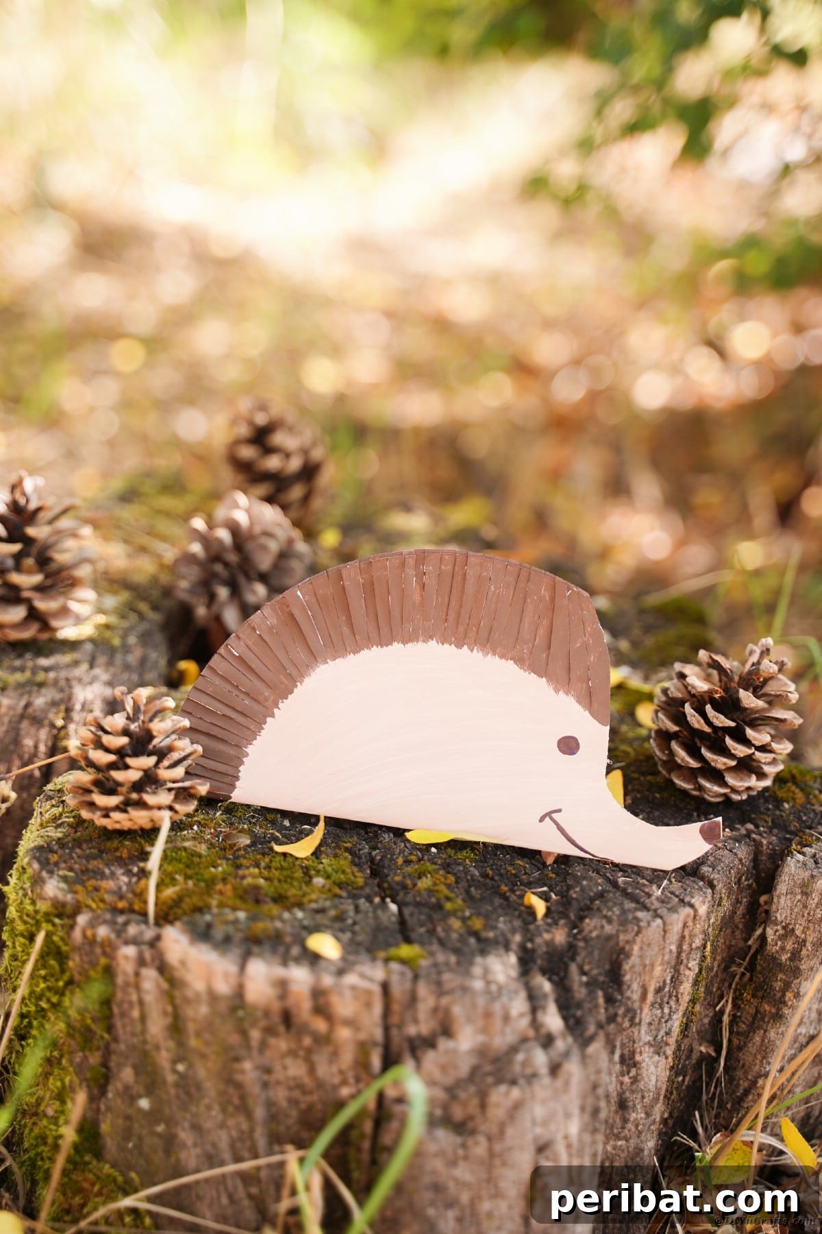 Hedgehog craft sitting on moss and pinecone covered stump