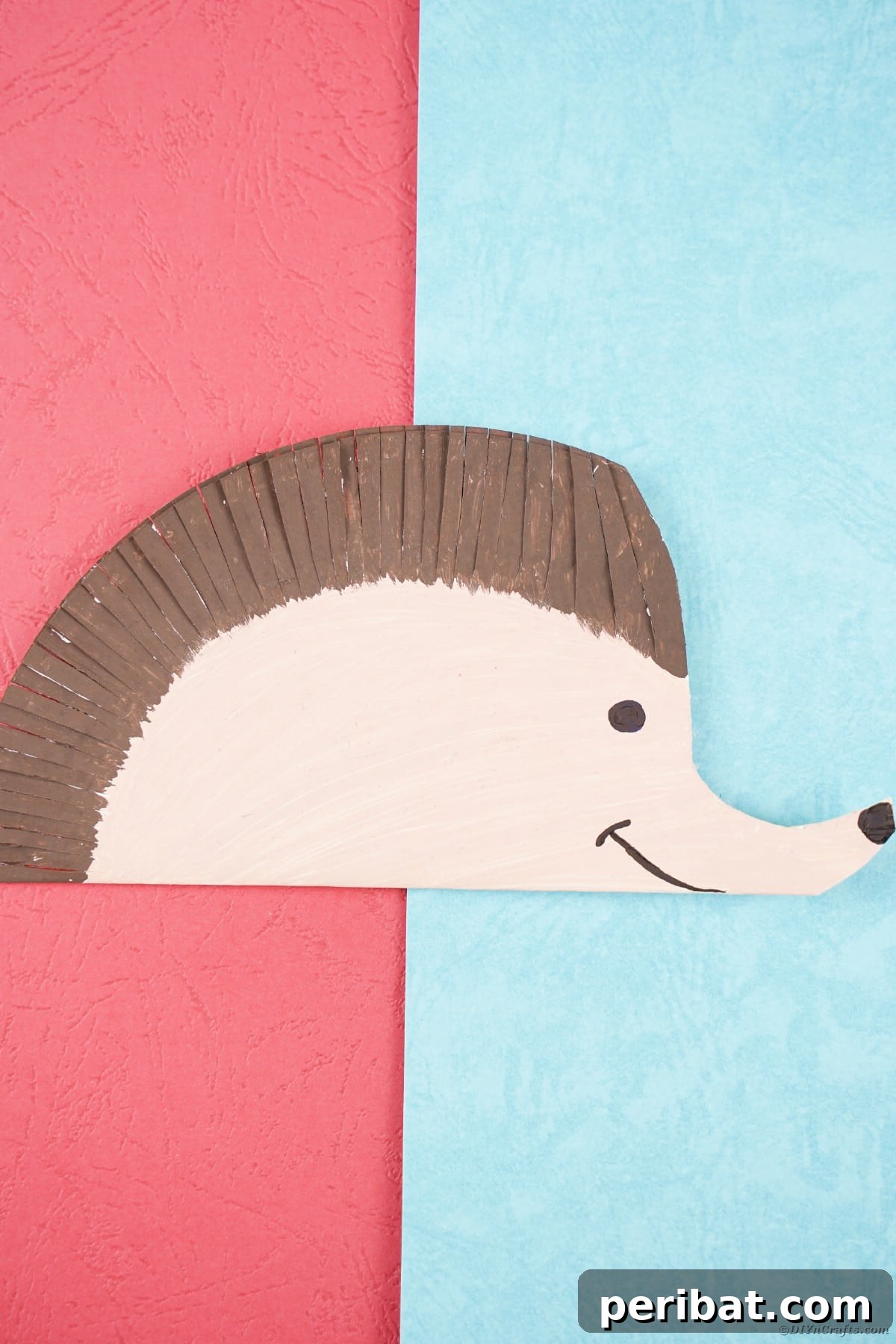 Paper plate hedgehog laying on pink and blue paper
