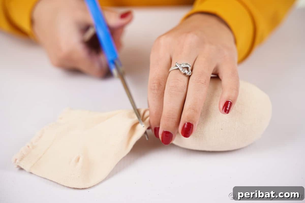 Effortless No-Stitch Fabric Hedgehog Creation 12 Scissors meticulously trim the excess fabric from the end of a stuffed sock, secured with a rubber band, finalizing the hedgehog's body shape.