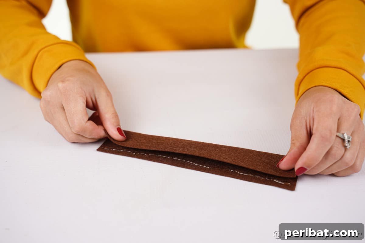 Effortless No-Stitch Fabric Hedgehog Creation 13 Hands carefully fold a piece of brown felt in half, preparing it for the next step in creating the hedgehog's textured spikes.