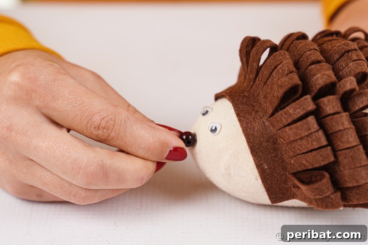 Effortless No-Stitch Fabric Hedgehog Creation 17 A hand carefully glues a small bead onto the front tip of a stuffed sock, creating the nose for the no-sew fabric hedgehog.