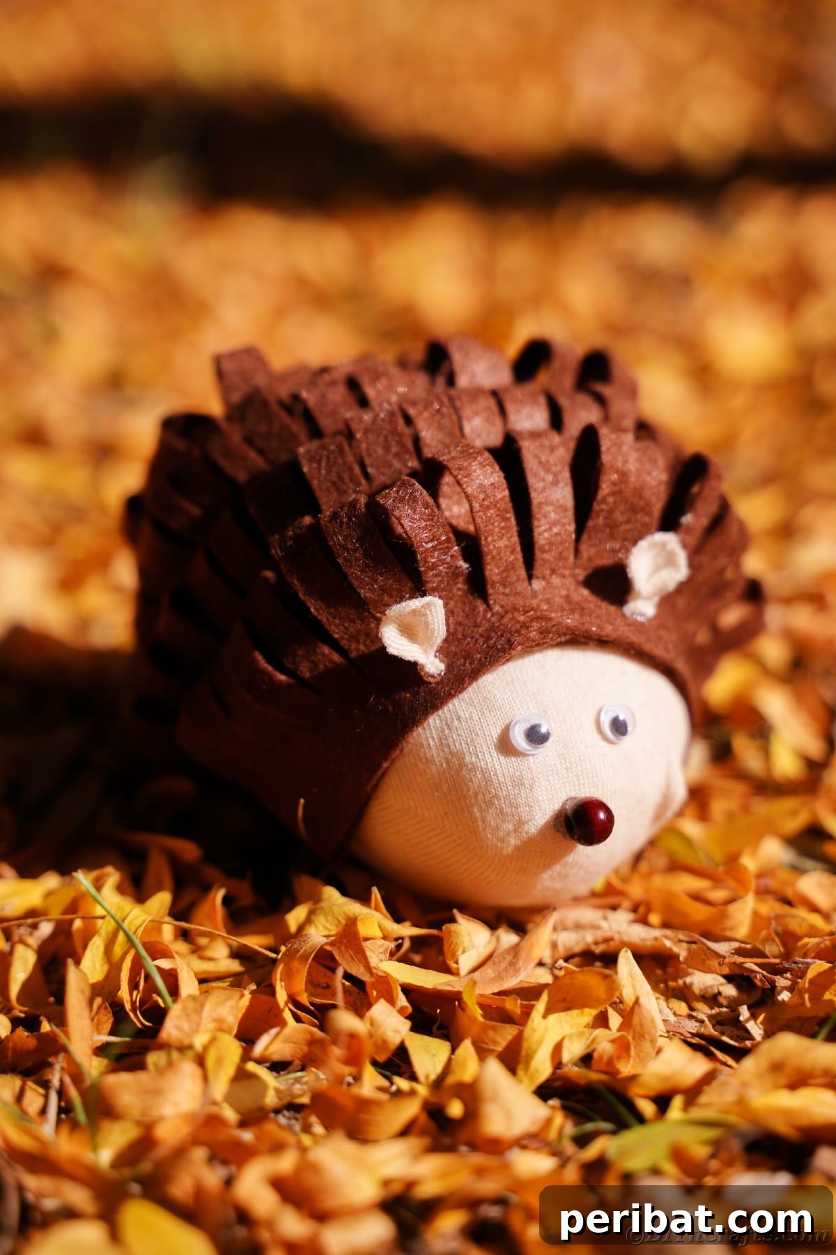 Effortless No-Stitch Fabric Hedgehog Creation 21 A charming brown and tan fabric hedgehog rests gracefully on a bed of golden yellow leaves, showcasing its cozy, autumnal appeal.