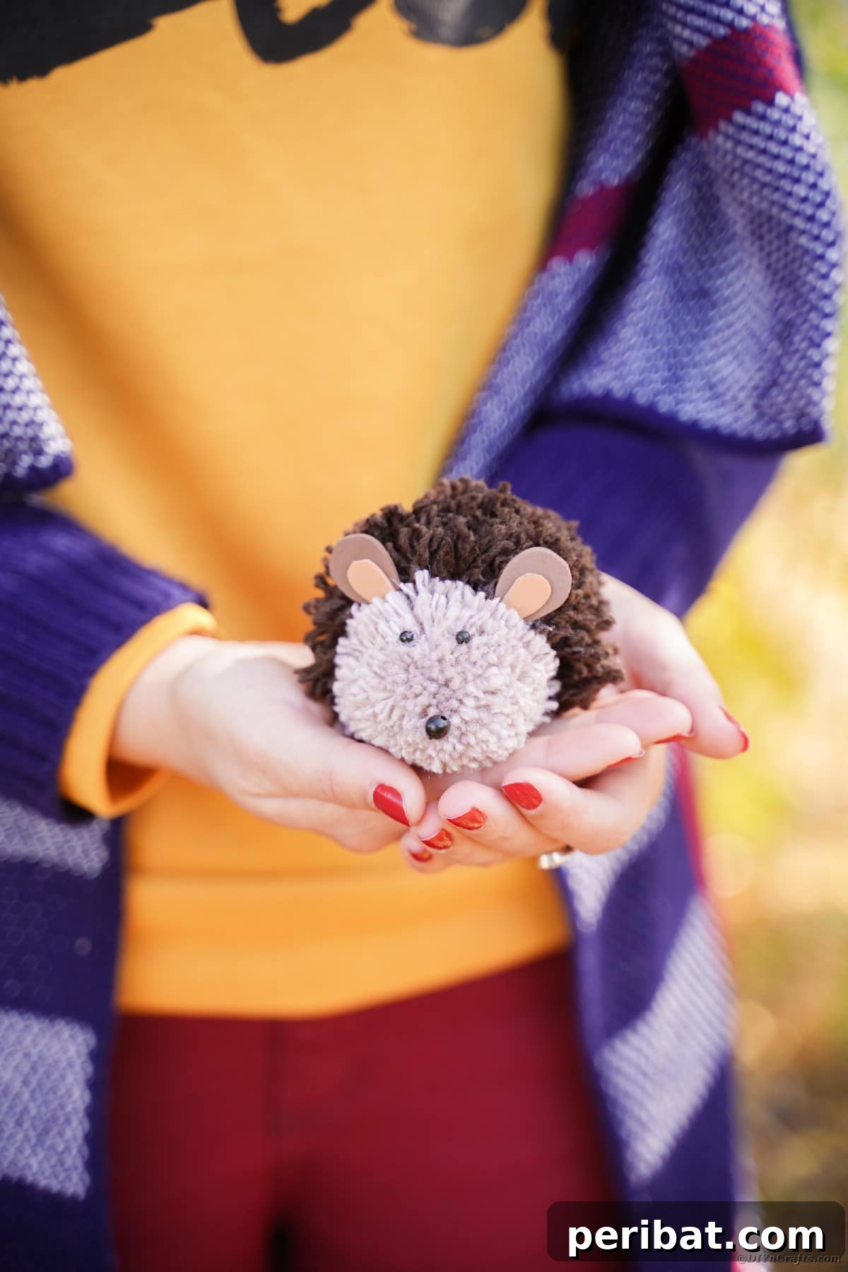 Adorable Pom Pom Hedgehog Fall Craft for Kids 2 Woman in orange shirt holding a fuzzy, brown DIY pom pom hedgehog toy