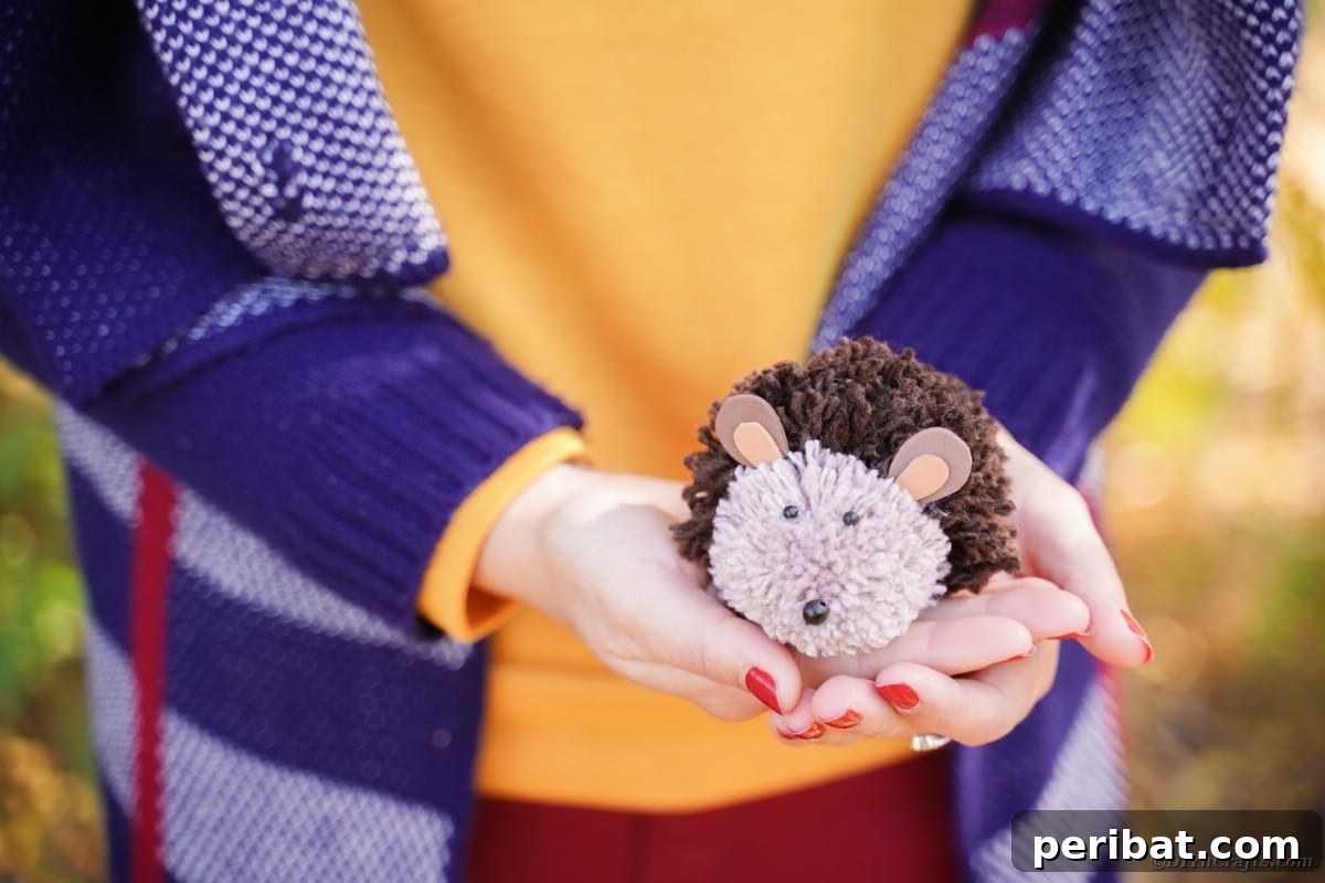 Adorable Pom Pom Hedgehog Fall Craft for Kids 10 Woman in blue jacket gently holding a finished brown pom pom hedgehog craft in her hands