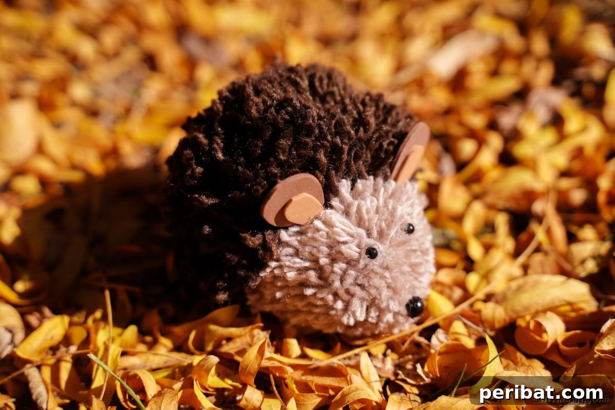 Adorable Pom Pom Hedgehog Fall Craft for Kids 3 Brown pom pom hedgehog resting on a bed of vibrant autumn leaves