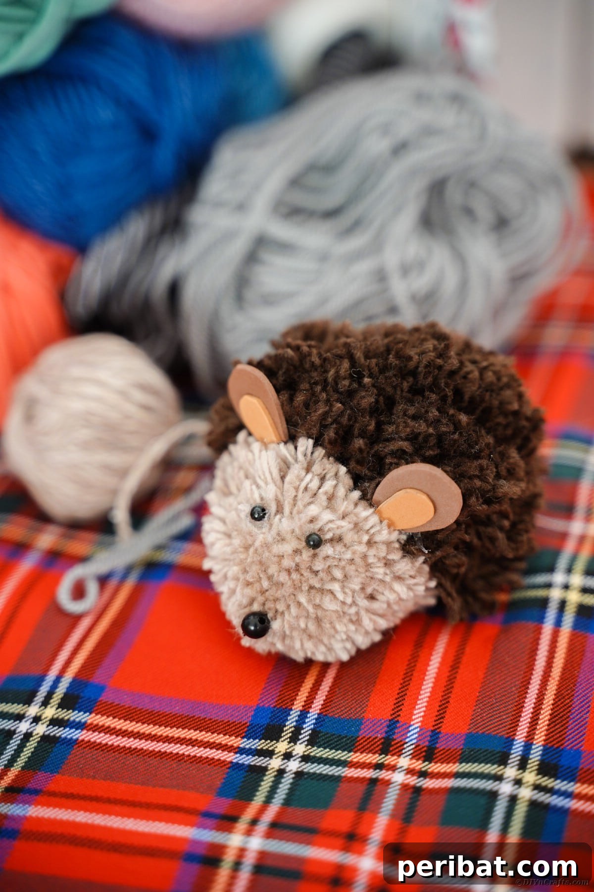 Adorable Pom Pom Hedgehog Fall Craft for Kids 4 Handmade pom pom hedgehog resting on a red and blue plaid blanket