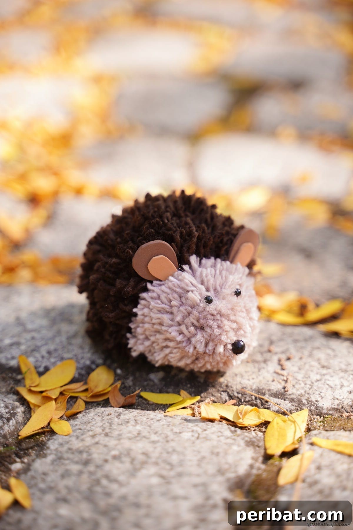 Adorable Pom Pom Hedgehog Fall Craft for Kids 12 Cobblestone path adorned with a cute yarn hedgehog and scattered fallen leaves, evoking an autumnal scene