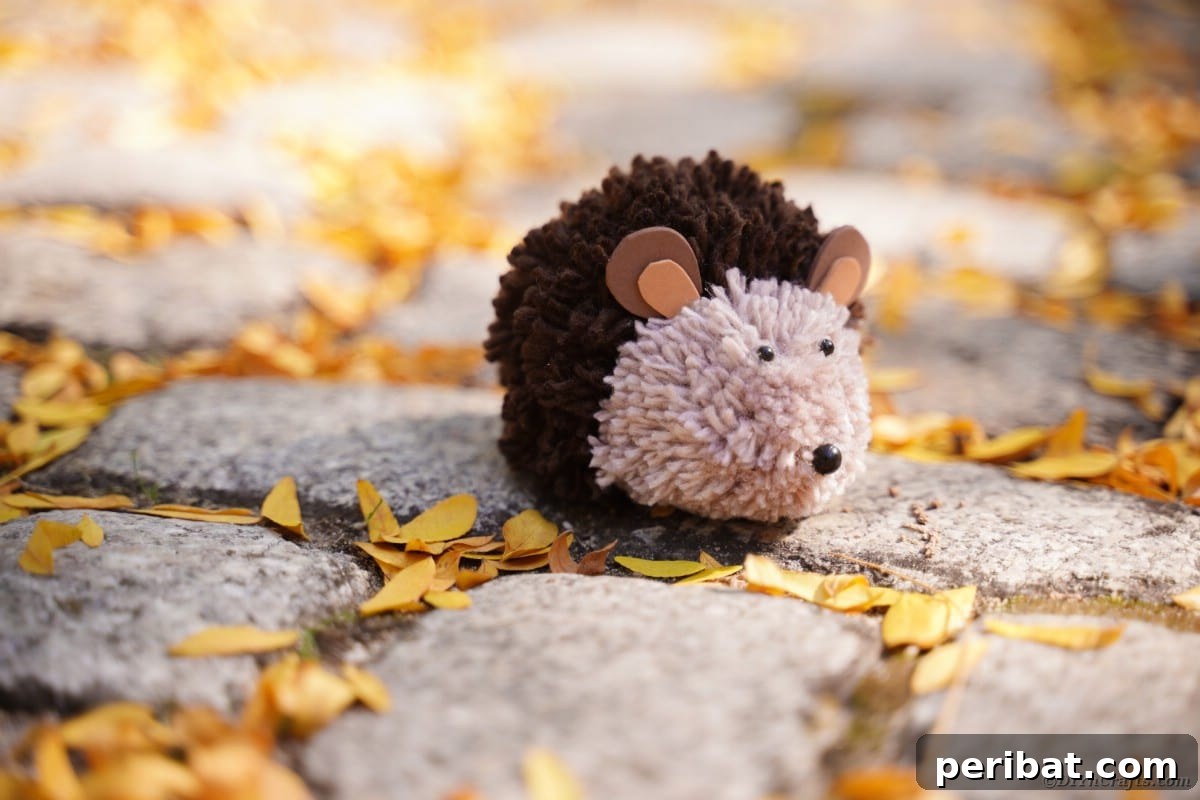 Adorable Pom Pom Hedgehog Fall Craft for Kids 5 Handmade brown pom pom hedgehog on cobblestone with scattered fallen leaves