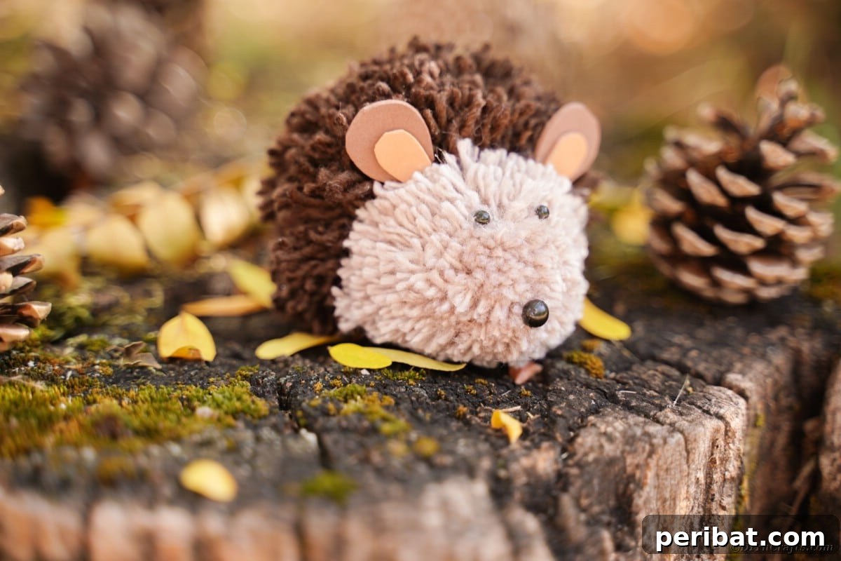 Adorable Pom Pom Hedgehog Fall Craft for Kids 6 Soft brown yarn pom pom hedgehog on top of a moss-covered tree stump