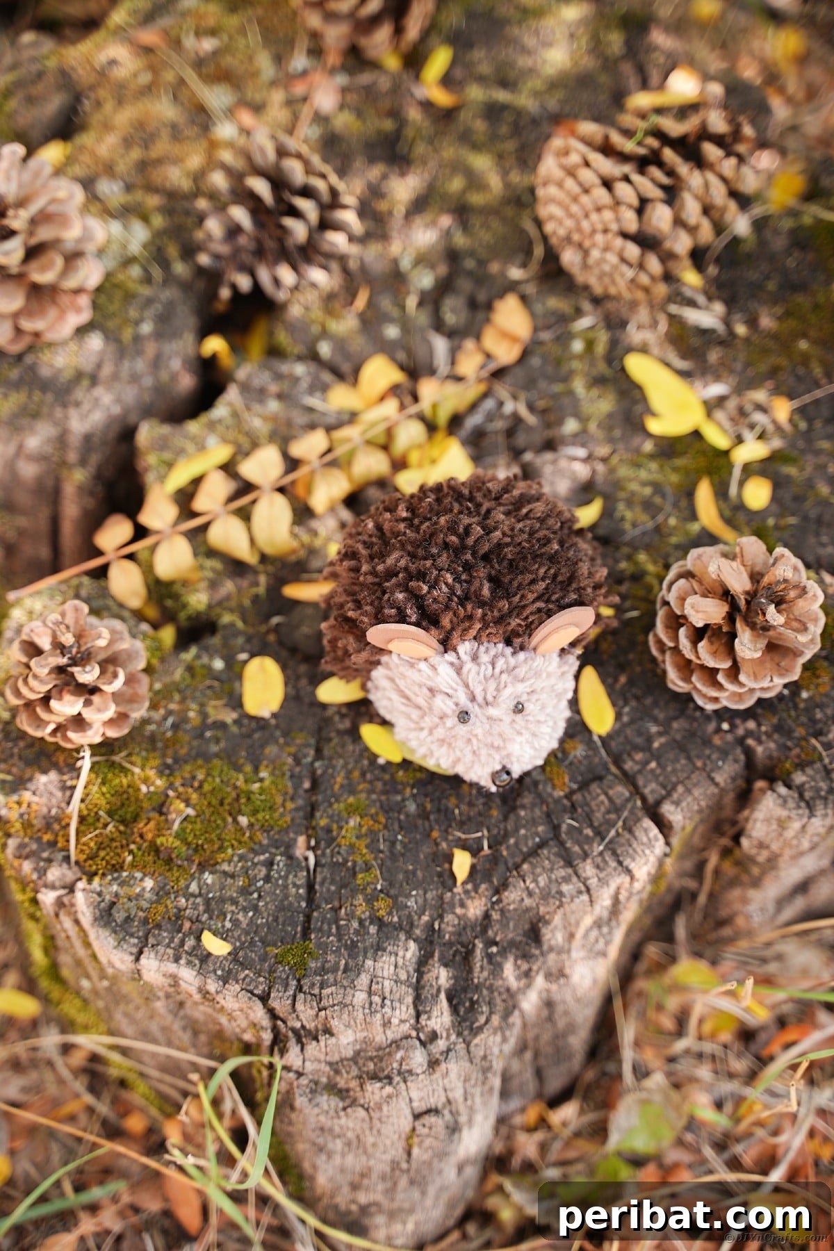 Adorable Pom Pom Hedgehog Fall Craft for Kids 7 Close-up of a brown yarn hedgehog resting on a moss-covered stump