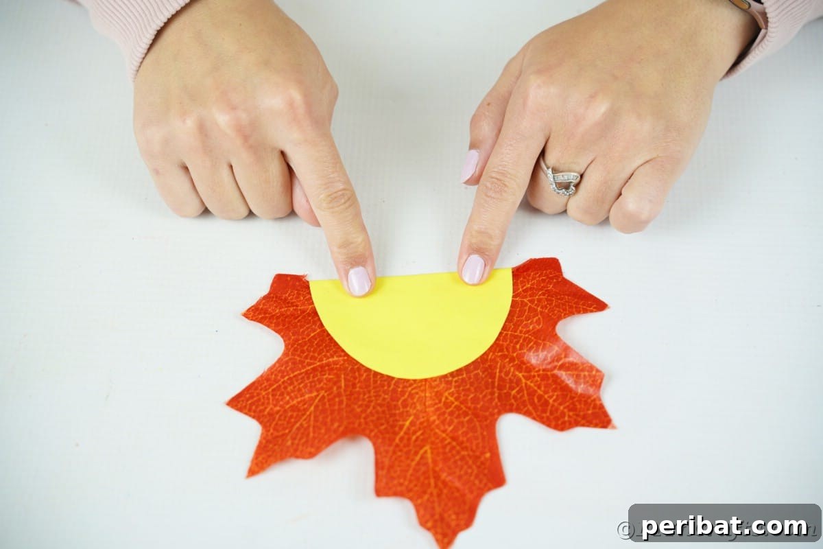 Hands holding yellow paper circle on top of artificial orange leaf ready for gluing