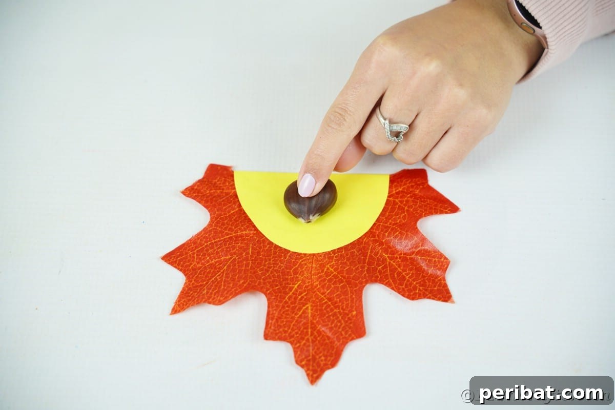 Hand gluing nut shell onto yellow paper on leaf