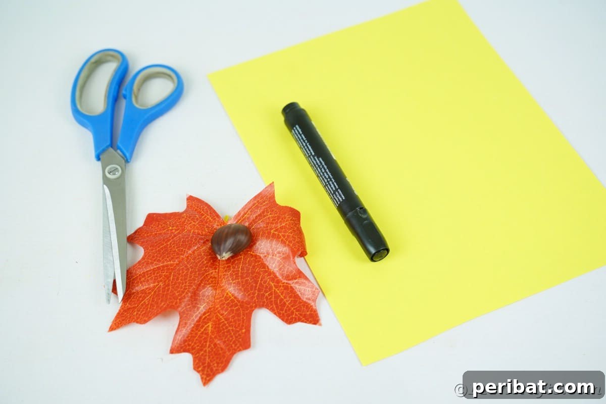 Orange fake leaf and yellow paper with marker and scissors on white table with craft supplies