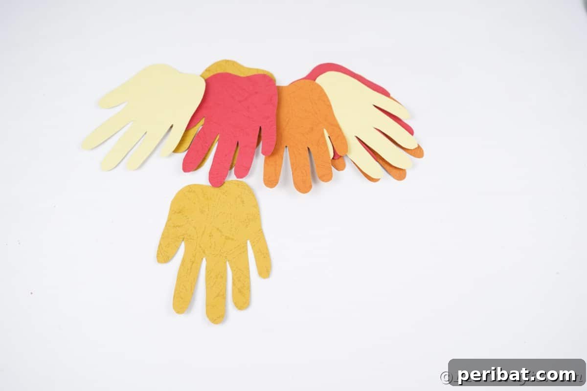 A neatly arranged pile of colorful paper handprints on a white table, ready for assembly
