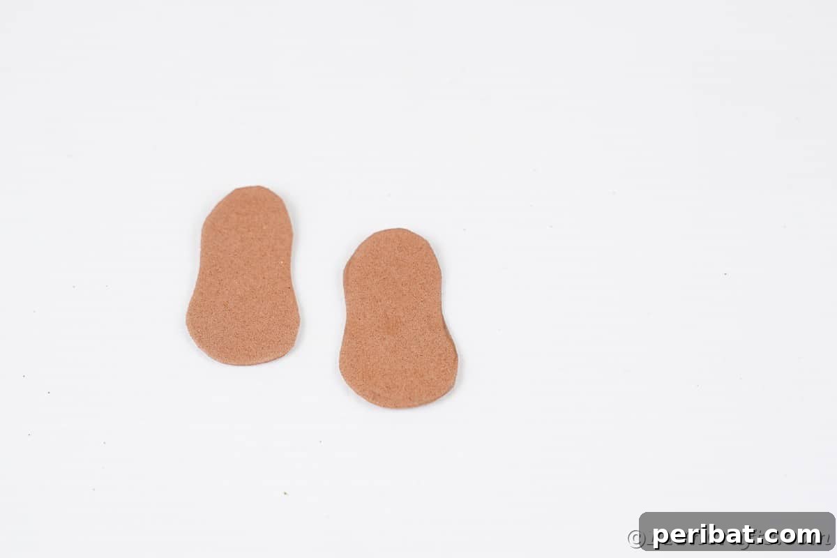 Two brown foam paper cutouts, shaped like small feet, placed on a clean white table