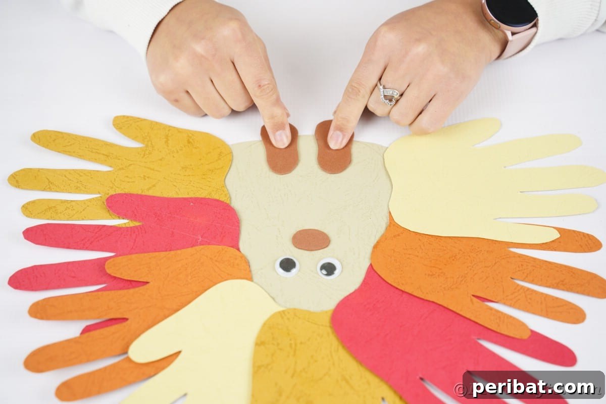 Fingers gently holding a foam foot piece against the bottom of the paper hedgehog, preparing to glue it in place