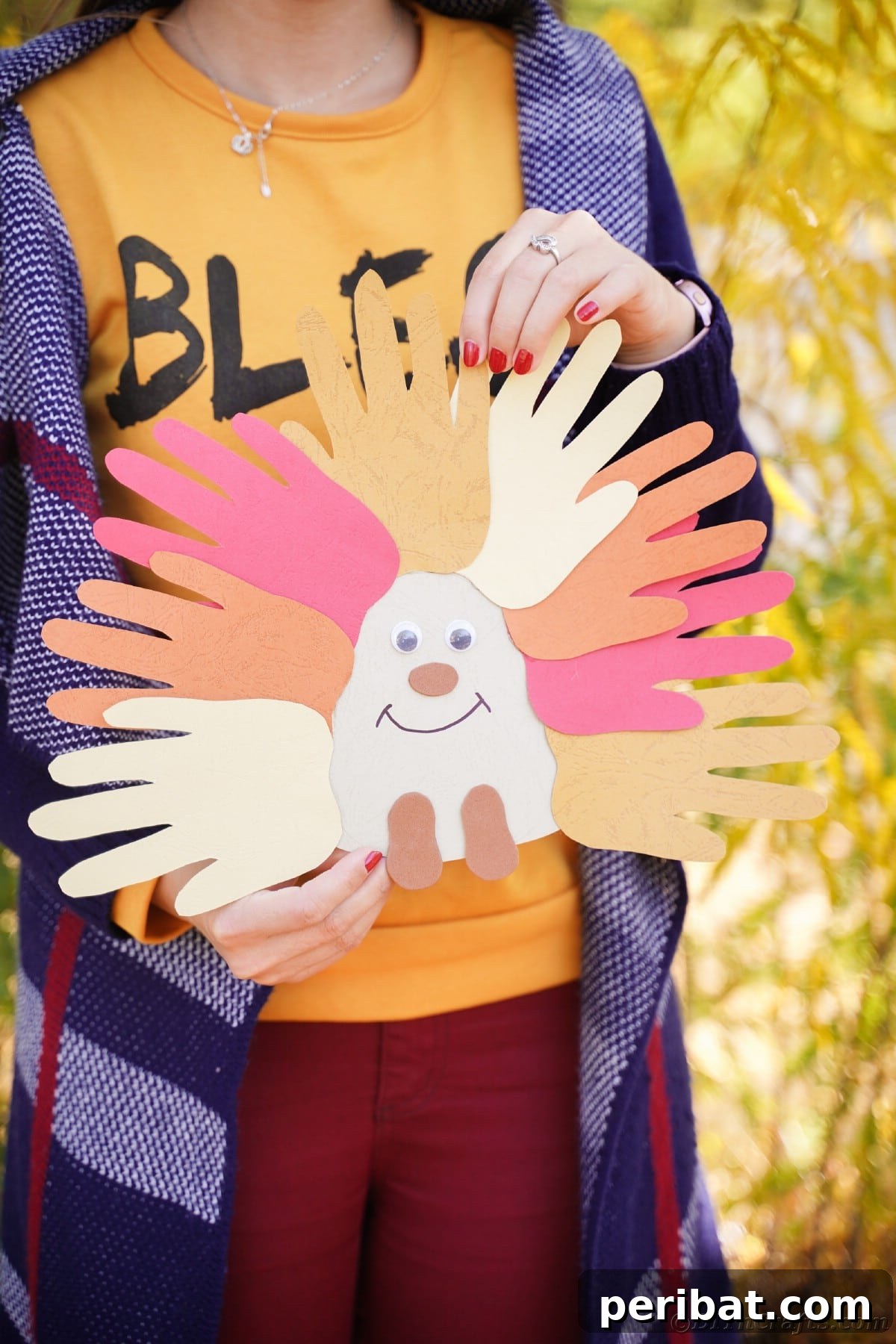 A woman in an orange shirt gently holding a colorful handprint hedgehog craft, showcasing its detail