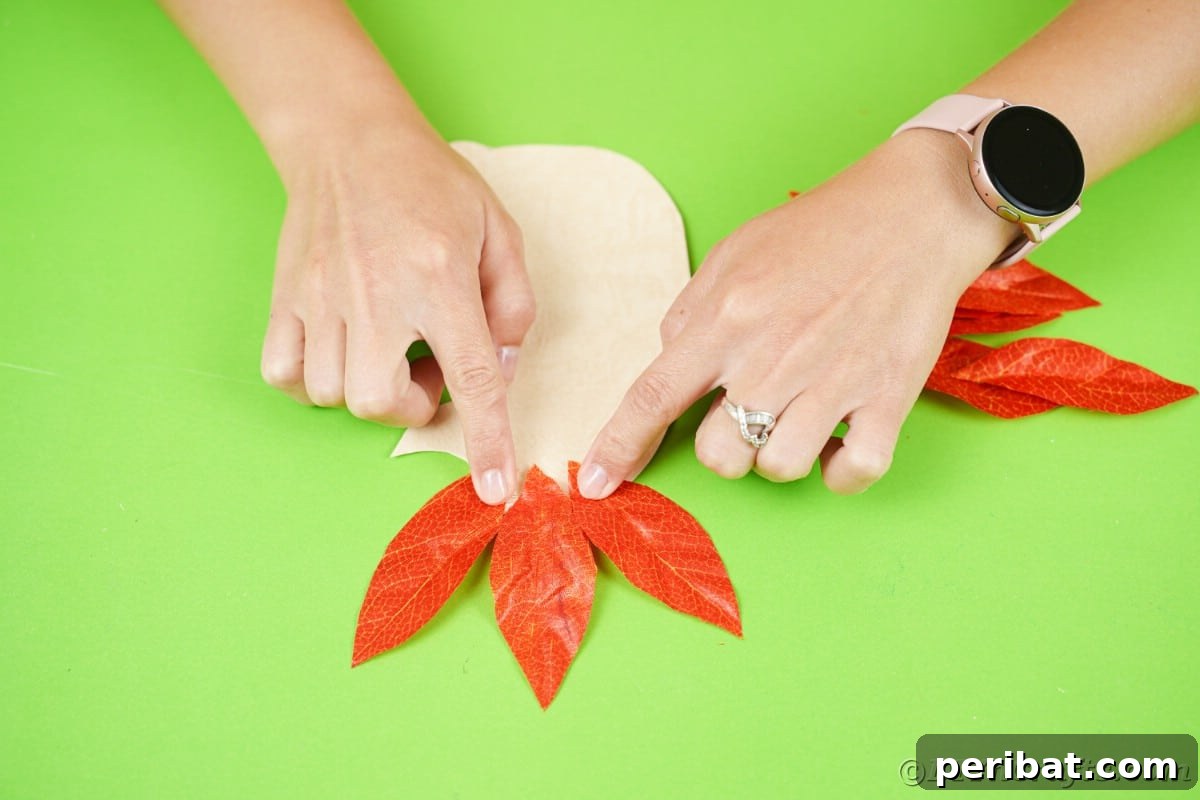Hands holding three fake leaves on top of cream paper, starting the quill layer.
