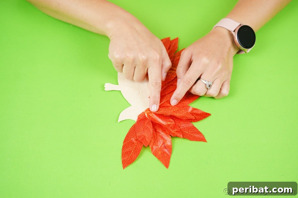 Hands holding fake leaves down on top of hedgehog shaped paper, completing the second layer.