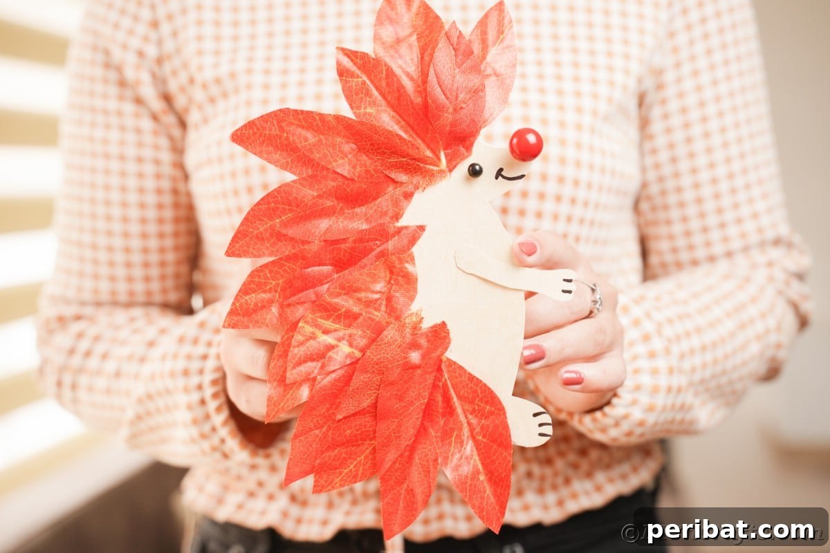 Hedgehog made of paper and fake leaves being held by woman, proudly presenting the finished craft.