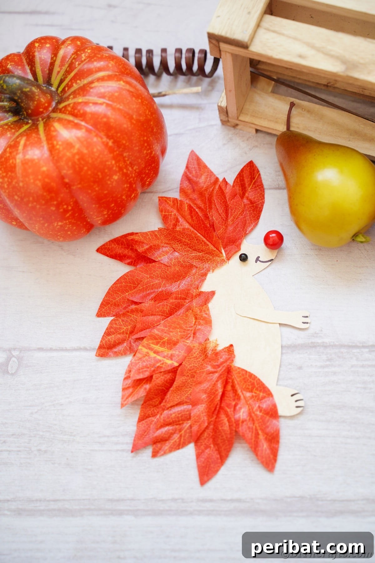 Paper and leaf hedgehog laying on white wood slat, a rustic display idea.